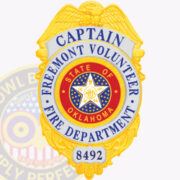 A vibrant image of a custom gold firefighter badge, featuring a detailed design with the title 'CAPTAIN' at the top, followed by 'FREEMONT VOLUNTEER' in blue. The center showcases a red circle with a star emblem and the words 'STATE OF OKLAHOMA' and 'FIRE DEPARTMENT.' The badge is adorned with intricate details, including eagle wings at the top, emphasizing its significance. This visual represents custom badges for Fire Department Badge Gold, illustrating the craftsmanship and personalization available for fire service roles.