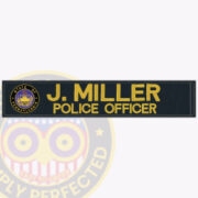 An image of a police embroidered name tape featuring a dark background with gold lettering. The name 'J. MILLER' is displayed prominently, followed by the title 'POLICE OFFICER.' On the left, there is a circular badge emblem representing the police department. This visual exemplifies police embroidered name tape, showcasing personalized identification for law enforcement uniforms.