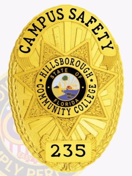 A distinctive custom metal badge in gold color with a safety pin attachment, designed for Hillsborough Community College. The badge prominently displays "CAMPUS SAFETY" along with a star emblem and the identifier "235," symbolizing authority and commitment to campus safety.