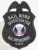 An elegant depiction of a custom metal badge in black color, showcasing a detailed shield shape adorned with the title “Bail Bond Investigator,” designed with a safety pin attachment for easy fastening to uniforms or clothing.