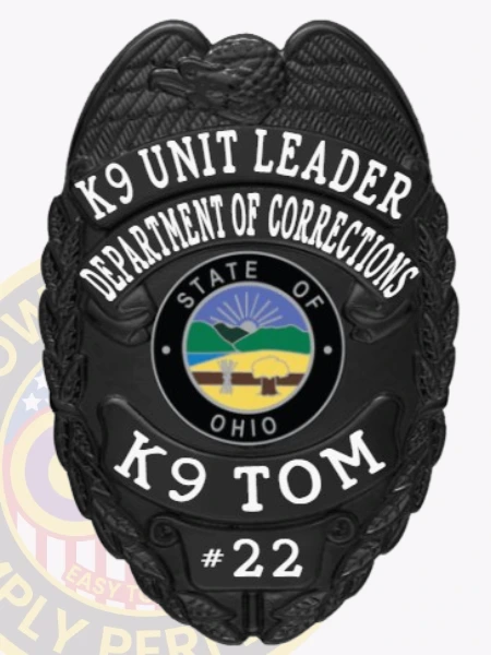 Featuring a polished custom metal badge in black color, this design includes a shield shape with "K9 UNIT LEADER," "DEPARTMENT OF CORRECTIONS," and "K9 TOM" clearly inscribed around a central emblem representing Ohio, along with the number "#22." The badge is completed with a safety pin attachment for easy application on uniforms.
