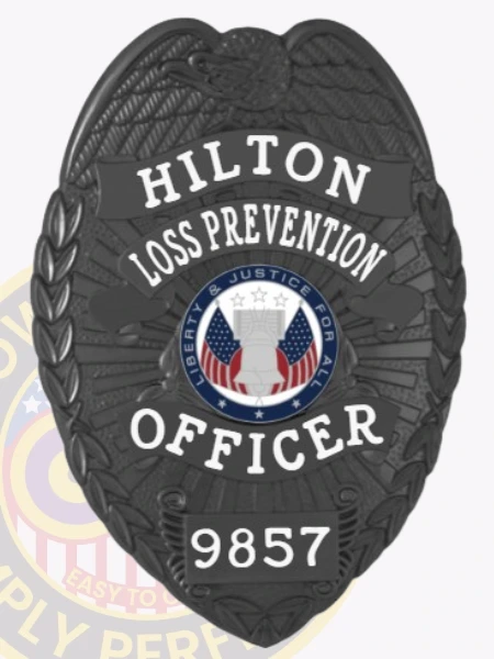 Featuring a custom metal badge in black color, this design highlights the title "HILTON LOSS PREVENTION OFFICER" and includes a decorative emblem at the center. The badge displays the identifier 9857 and is equipped with a safety pin attachment for convenient wear, making it ideal for official use.
