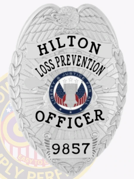 An eye-catching custom metal badge in silver color, adorned with "HILTON LOSS PREVENTION OFFICER" prominently displayed above a central emblem symbolizing liberty and justice. The badge features a unique identification number, 9857, and comes with a safety pin attachment for secure placement.