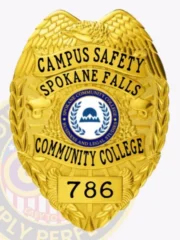 Featuring a detailed custom metal badge in gold color with a secure safety pin attachment, this badge reads "CAMPUS SAFETY SPOKANE FALLS." The intricate design includes the Spokane Community College logo, emphasizing its role in ensuring safety on campus.