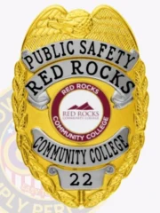 A striking custom metal badge in gold color with elegant silver panels and a safety pin attachment, designed for Red Rocks Community College. The badge displays bold lettering of "PUBLIC SAFETY RED ROCKS" along with a circular emblem, perfectly combining functionality and style.
