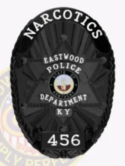 Black oval custom metal badge for Eastwood police narcotics unit displaying a raised six-point star with intricate detailing, central colorful Kentucky state emblem, white text banners reading NARCOTICS at the top and EASTWOOD POLICE DEPARTMENT around the seal, plus a black number plate 456 at the base; badge includes safety pin attachment.