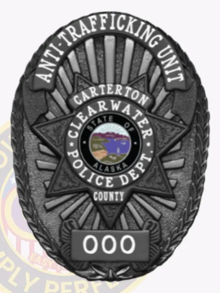 Oval-shaped custom black metal badge for Clearwater Police Anti-Trafficking Unit showing a star emblem with the Alaska state seal in the center, surrounded by white text including "ANTI-TRAFFICKING UNIT," "CARTERTON," "CLEARWATER POLICE DEPT.," and "COUNTY," with a numbered plate "000" below, held by a safety pin.