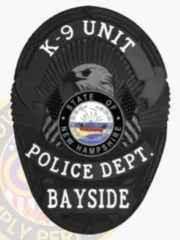 Black oval custom metal badge for Bayside Police K-9 Unit, featuring an eagle's head silhouette above the circular New Hampshire state seal, surrounded by white text stating "K-9 UNIT" on top, "POLICE DEPT." in the center, and "BAYSIDE" at the base, fastened with a safety pin.
