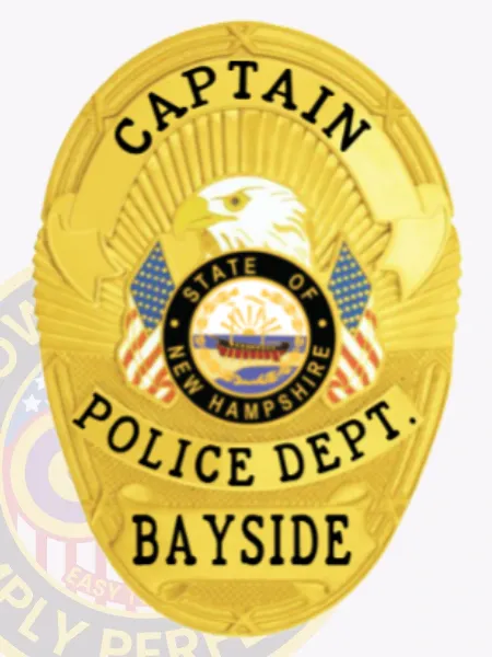 Oval-shaped custom gold metal badge for Bayside Police Captain showcasing an eagle with yellow beak above the New Hampshire state seal, flanked by American flags, labeled with black text "CAPTAIN," "POLICE DEPT.," and "BAYSIDE," secured by a safety pin.