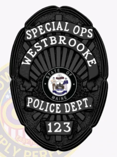Oval-shaped black metal badge customized for Westbrooke police special ops, showing a sunburst pattern on a matte black base, white scrolls with bold lettering SPECIAL OPS at the top, WESTBROOKE in the middle, POLICE DEPT. below, and the number 123 on a rectangular plaque at the bottom, plus a colorful Maine state emblem at the center, featuring a safety pin fastener.