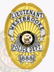Gold oval custom metal badge designed for Westbrooke police lieutenant displaying a radiant gold background with white banners carrying the text LIEUTENANT, WESTBROOKE, POLICE DEPT., a central Maine state seal in black and gold, and the numeric ID 888 on a silver plaque near the bottom, attached with safety pin.