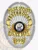 Silver oval custom metal badge for Westbrooke police officer, displaying a polished silver sunburst background behind a black and gold State of Maine seal, with gold banners stating POLICE OFFICER, WESTBROOKE, POLICE DEPT., and a number 999 on a gold plaque at the bottom, featuring a safety pin fastening.