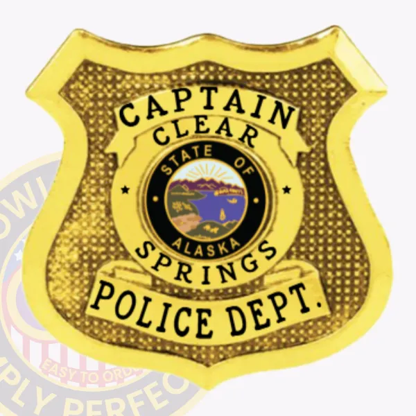 Custom-designed gold shield metal badge for Clear Springs police captain displaying clear black text on three curved banners and a detailed Alaska state seal at the center, secured by a traditional safety pin attachment.
