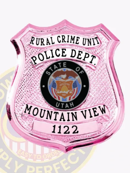 Custom BCAM pink shield metal badge for Mountain View police rural crime unit with shiny pink finish and safety pin attachment, highlighting RURAL CRIME UNIT in black uppercase letters on a white arched panel at the top, POLICE DEPT. beneath it, the State of Utah seal prominently displayed below, and MOUNTAIN VIEW 1122 printed on white strips near the bottom.