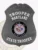 A sleek custom badge in black, designed in the shape of a shield. The top displays the word "TROOPER" followed by "MARYLAND," while the bottom reads "STATE TROOPER." The central emblem features the state seal of Maryland, depicted within a black circle and including images of two soldiers against a vibrant backdrop. The matte finish adds a touch of sophistication, making this custom badge in black an emblem of authority and service.