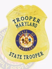 A custom badge in gold with blue lettering, featuring the word "TROOPER" at the top and "MARYLAND" just below it. The badge displays a central emblem that reads "STATE OF MARYLAND," surrounded by decorative details. At the bottom, "STATE TROOPER" is prominently featured, enhancing its official appearance. The badge is designed with a polished gold finish that reflects light beautifully.
