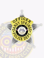 Five-point star badge in silver metal for Sandy Springs Police Officer, showing "Officer Sandy Springs Police Dept." on a yellow circular banner around the central Georgia state seal, with safety pin fastening.