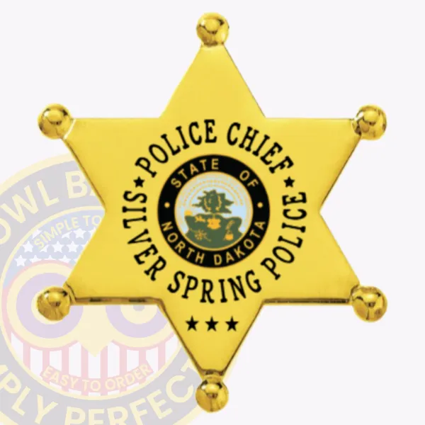 Custom gold metal badge in a 6 point star shape for Silver Spring Police Chief, with smooth star points and ball-shaped tips, a central blue and gold North Dakota seal, bold black letters around it spelling "POLICE CHIEF SILVER SPRING POLICE," and the initials "ND" at the bottom, attached by safety pin.