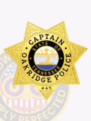 Gold custom 7 point star metal badge for Oakridge Police Captain, featuring textured ornamental designs on the star surface, clear black lettering stating "CAPTAIN," "OAKRIDGE POLICE," and identification number "445," finished with a safety pin clasp.