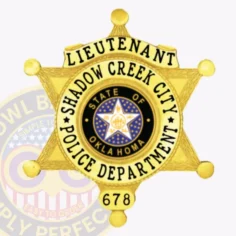 Gold metal badge shaped as a 6 point star for shadow creek city police lieutenant, displaying black lettering on a gold banner at the top, the oklahoma state seal in the center encircled by the department name, with textured leaf designs on the star points and a safety pin fastener.