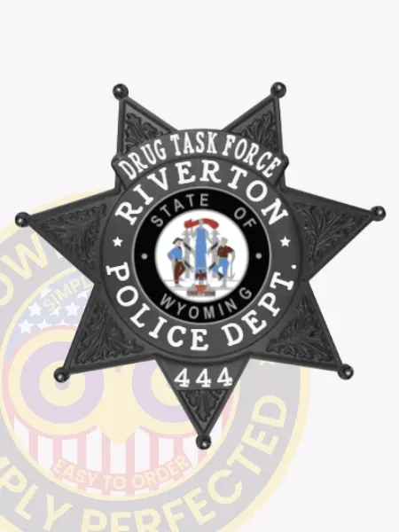 Custom black 7 point star metal badge designed for Riverton police the drug task force, featuring elaborate leaf embossing on every star point, a central circular Wyoming state emblem, and prominent white lettering around it reading “Drug Task Force Riverton Police Dept” with the number “444,” attached with a safety pin.