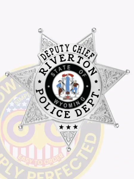 Metal badge in silver shaped as a 7 point star for Riverton police the deputy chief, with raised leaf engravings on each star tip, a central colorful Wyoming state seal, and bold black text surrounding it that says “Deputy Chief Riverton Police Dept,” fastened by a safety pin.
