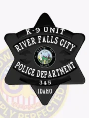 Black metal badge shaped as a 6 point star for the K9 Unit of River Falls City Police Department, Idaho, displaying white embossed text including unit name and department details, centered by the official Idaho state seal, and equipped with a safety pin for fastening.