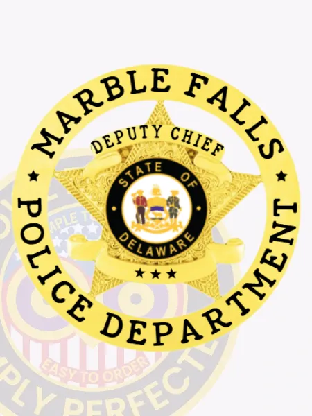 Circular gold badge displaying a five-point star with intricate engraving, surrounded by the text "Marble Falls Police Department" in black, and a curved banner over the star reading "Deputy Chief," featuring the State of Delaware emblem in the center, designed with a safety pin fastener.