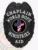 This elegant custom metal badge in black color with a safety pin attachment displays the words "CHAPLAIN," "WORLD HOPE MINISTRIES," and "AID." The badge's centerpiece features a bold black circle with a colorful cross, reflecting commitment and support.