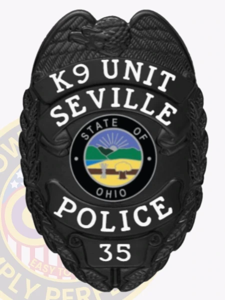 A striking custom metal badge in black with white lettering, shaped like a shield and featuring detailed engravings. The badge displays "K9 UNIT" at the top and "SEVILLE POLICE" below, both in bold white letters for high visibility. At the center, the state seal of Ohio is showcased, depicting a rising sun over a serene landscape within a circular black backdrop. The badge also includes the number "35" at the bottom. The matte finish of this custom metal badge in black with white lettering emphasizes its professional and authoritative presence, symbolizing the important role of K9 officers in law enforcement.