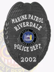 Riverdale Police Marine Patrol custom metal badge in matte black, featuring a prominent eagle design at the top, bold white text reading "MARINE PATROL," "RIVERDALE," and "POLICE DEPT." encircling the New York State seal in the center, with the date "2002" on a lower shield plate and a safety pin fastener on the back.