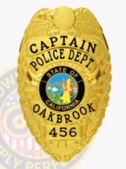 Oakbrook Police Department Captain gold eagle badge with raised eagle on top, black lettering surrounding the California state seal, “CAPTAIN POLICE DEPT. OAKBROOK” text and “456” identification number, attached by a safety pin.