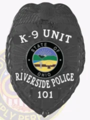 Matte black metal badge for Riverside Police K-9 Unit featuring an eagle perched on top, white embossed text on black background reading "K-9 UNIT," "RIVERSIDE POLICE," and badge number "101," surrounding the official Ohio state seal, finished with a safety pin attachment.