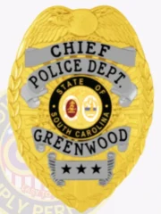 Gold metal badge for Greenwood Police Chief displaying an eagle motif atop the shield, silver banners with bold black text reading "CHIEF," "POLICE DEPT.," and "GREENWOOD," surrounding the colorful South Carolina state insignia, finished with three black stars on a silver bottom plate and secured with a safety pin.