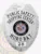 A striking custom metal badge in silver color with a safety pin attachment highlights the titles "PUBLIC SAFETY" and "SHOPPING CENTER." The design includes a colorful depiction of the Maryland state seal at the center, framed by elegant silver accents.