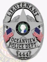 Silver oval police badge for Oceanview lieutenant featuring a large five-point star in the center containing the State of Washington seal, black letters LIEUTENANT arched along the top, OCEANVIEW POLICE DEPT. beneath the star, badge number 444 on a plate at the bottom, accompanied by two American flags, equipped with safety pin.