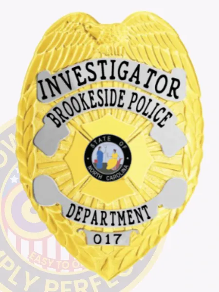 A detailed image of a custom metal badge in gold with silver panels, prominently featuring the title "INVESTIGATOR" at the top. The badge displays "BROOKESIDE POLICE" and "DEPARTMENT," along with the state emblem of North Carolina, identifying it with badge number 017. The safety pin attachment is clearly visible for secure wear.