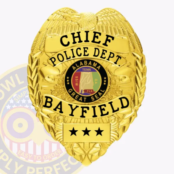 A detailed view of a custom metal badge in gold color featuring an eagle design at the top. The badge prominently displays the title "CHIEF" and includes the text "POLICE DEPT. BAYFIELD" along with the Alabama state seal in the center. The badge number is marked with stars at the bottom, and it is designed with a safety pin attachment for secure fastening.