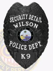 Detailed custom black police badge for Wilson Security Detail, featuring an eagle crest, white letters stating "SECURITY DETAIL WILSON POLICE DEPT." around the state seal of Florida, and a "K9" label on the bottom plate, attached with a safety pin.