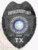 A polished custom metal badge in black, prominently displaying "ENFORCEMENT UNIT" at the top. The badge includes a central star emblem, surrounded by the text "METROPOLITAN POLICE DEPARTMENT" and "THE STATE OF TEXAS." Intricate patterns enhance its design, with laurel leaves adorning the edges. The badge is marked with the number "80" and "TX" at the bottom, representing its official status as a personalized police badge.