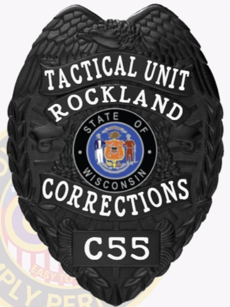 A custom metal badge in a sleek black color, shaped like a shield, representing the Tactical Unit of Rockland Corrections. The badge prominently features "TACTICAL UNIT" at the top, followed by "ROCKLAND" and "CORRECTIONS" in bold white letters. In the center, it showcases the state seal of Wisconsin, surrounded by decorative elements. The badge is labeled with the number "C55" at the bottom and includes a safety pin attachment on the back, allowing for secure wear by correctional officers, emphasizing its functional design and authority.