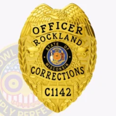 A close-up of a custom metal badge in a bright gold color, designed in the shape of a shield, representing the rockland corrections. The badge prominently features "officer" at the top, followed by "rockland" and "corrections" in bold lettering. In the center, it displays the state seal of wisconsin, surrounded by decorative elements. The badge is marked with the number "c1142" at the bottom and includes a safety pin attachment on the back, allowing for secure wear by correctional officers, emphasizing its practical design and significance.