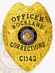 A custom metal badge in a vibrant gold color, shaped like a shield, representing the Rockland Corrections. The badge prominently displays "OFFICER" at the top, followed by "ROCKLAND" and "CORRECTIONS" in bold lettering. In the center, it features the state seal of Wisconsin, framed by intricate designs. The badge is labeled with the number "C1142" at the bottom and has a safety pin attachment on the back, allowing for secure wear by correctional officers, highlighting its practical design and authority.