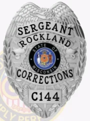 A custom metal badge in a polished silver color, shaped like a shield, representing the Rockland Corrections. The badge features "SERGEANT" prominently at the top, followed by "ROCKLAND" and "CORRECTIONS" in bold lettering. In the center, it displays the state seal of Wisconsin, surrounded by decorative elements. The badge is marked with the number "C144" at the bottom and includes a safety pin attachment on the back, allowing for secure wear by correctional staff, highlighting its practical design and authority.