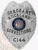 A custom metal badge in a polished silver color, shaped like a shield, representing the Rockland Corrections. The badge features "SERGEANT" prominently at the top, followed by "ROCKLAND" and "CORRECTIONS" in bold lettering. In the center, it displays the state seal of Wisconsin, surrounded by decorative elements. The badge is marked with the number "C144" at the bottom and includes a safety pin attachment on the back, allowing for secure wear by correctional staff, highlighting its practical design and authority.