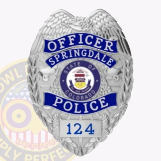 A close up custom metal badge in silver featuring the title "OFFICER" at the top, followed by "SPRINGDALE" in bold blue letters. The center showcases the state seal of Colorado, surrounded by decorative silver laurel leaves. The word "POLICE" is prominently displayed in blue at the bottom, with the number "124" on a silver panel below it. The badge has a polished silver finish with intricate detailing, highlighting its official and authoritative design.