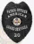 Detailed look at a custom metal badge in black color with safety pin attachment, featuring a shield design. The top inscription states "PATROL OFFICER," while "AMERICAN" is highlighted beneath it. The central area showcases the state seal of Arkansas, and "20" is displayed on a black panel at the bottom, reinforcing its official capacity.