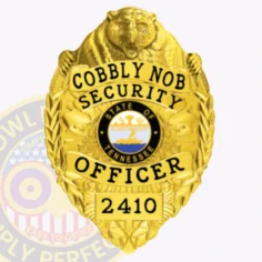 Close up image of a custom metal badge in gold, designed with a safety pin attachment. The badge reads "cobbly nob security" and "security officer" in bold lettering, surrounded by decorative motifs and a state emblem, illustrating its official purpose and elegant appearance.
