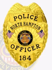 A bright custom metal badge gold, shaped like a shield with detailed engravings. The badge features "POLICE" at the top in bold black letters, followed by "NORTH HAMPTON" beneath it. In the center, the state seal of Utah is displayed within a circular design, flanked by two small American flags. Below the seal, "OFFICER" is prominently written, and the badge includes the number "184" at the bottom. The shiny gold finish of this custom metal badge gold highlights its authority and professionalism, making it an impressive symbol of law enforcement pride.