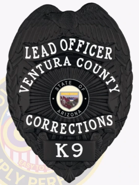 A custom metal badge in a sleek black color, shaped like a shield, representing the Ventura County Corrections. The badge prominently features "LEAD OFFICER" at the top, followed by "VENTURA COUNTY" in bold letters. The center displays the state seal of Arizona, surrounded by decorative patterns. At the bottom, it reads "CORRECTIONS" and "K9," indicating its specific role. This badge includes a safety pin attachment on the back, ensuring secure wear by correctional officers, emphasizing its importance and design.